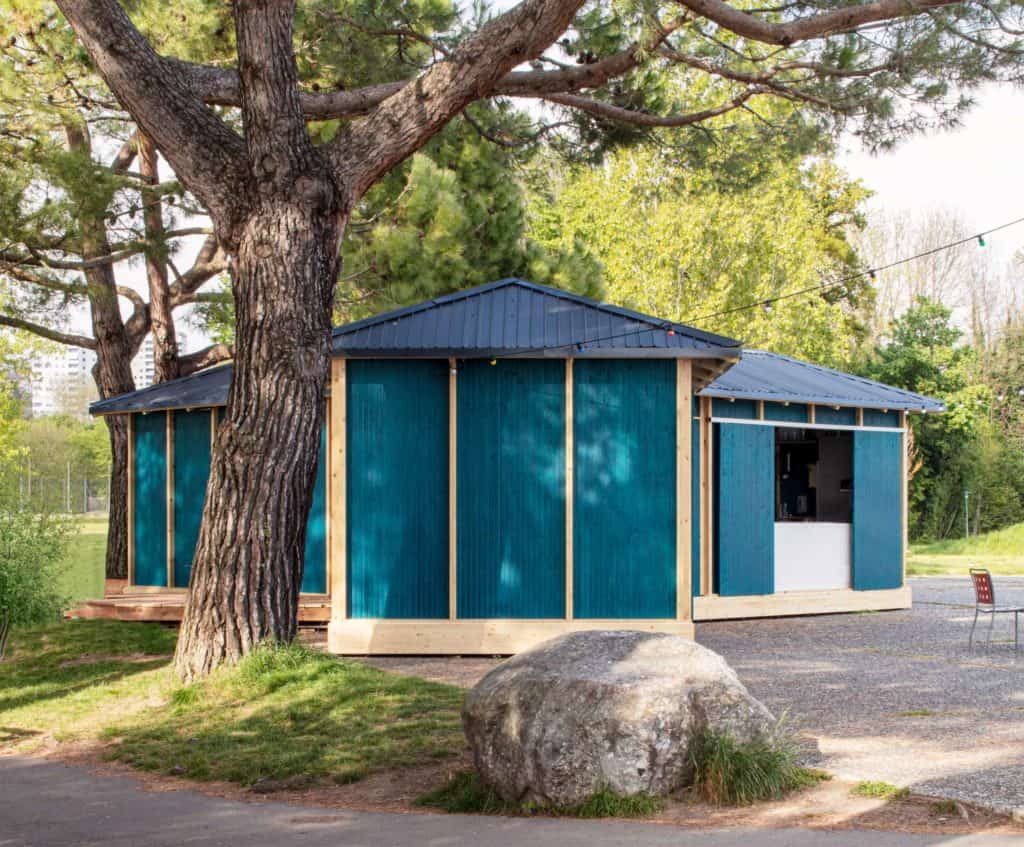 Cabane en bois bleu dans un parc avec grands arbres et rocher.