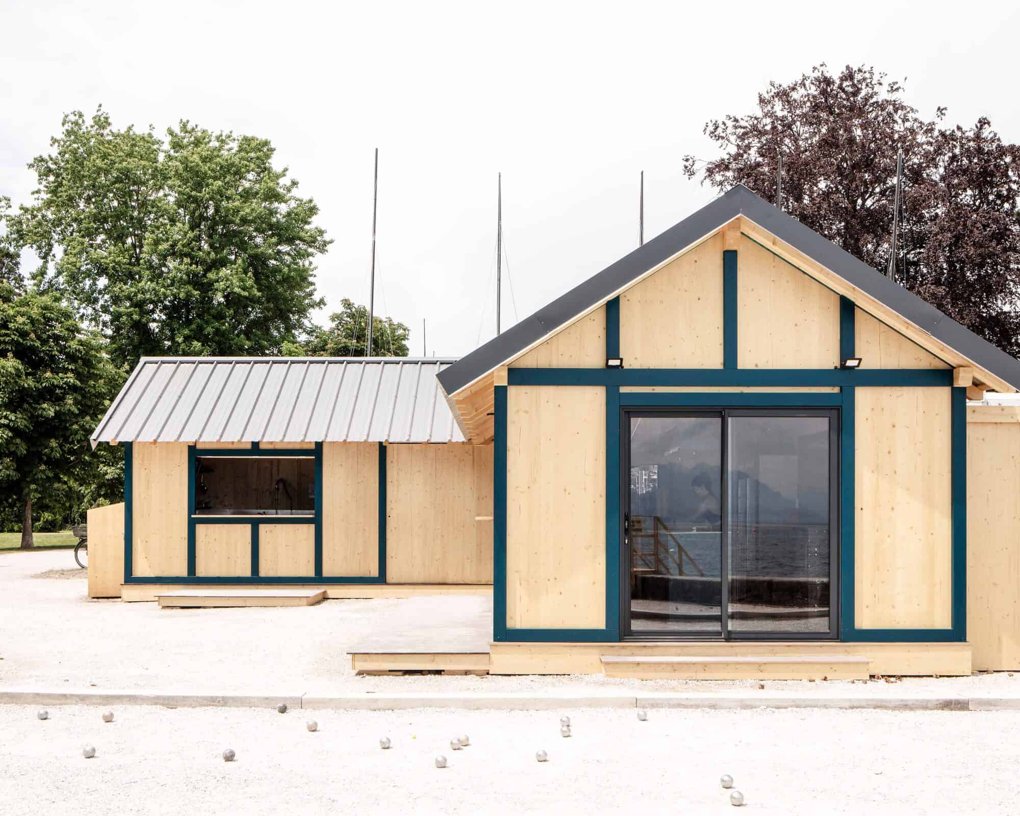 Cabane en bois moderne avec grandes fenêtres et toit en métal gris.