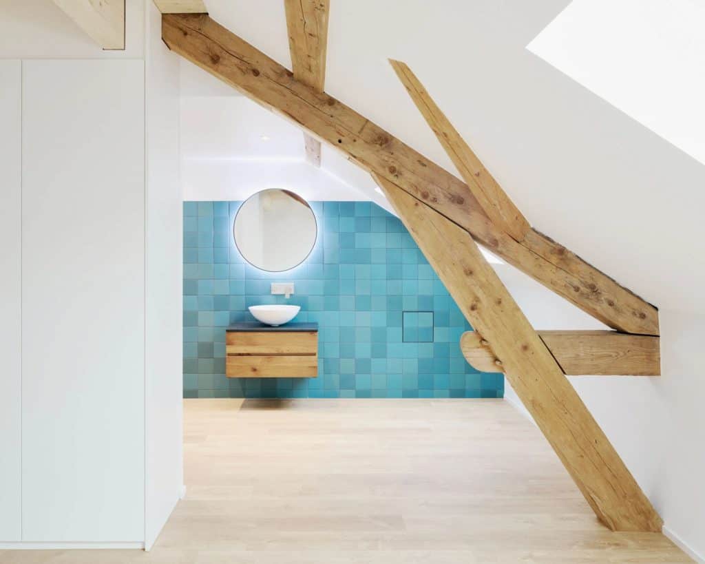 Intérieur moderne d'une salle de bain sous un toit en pente avec poutres en bois.